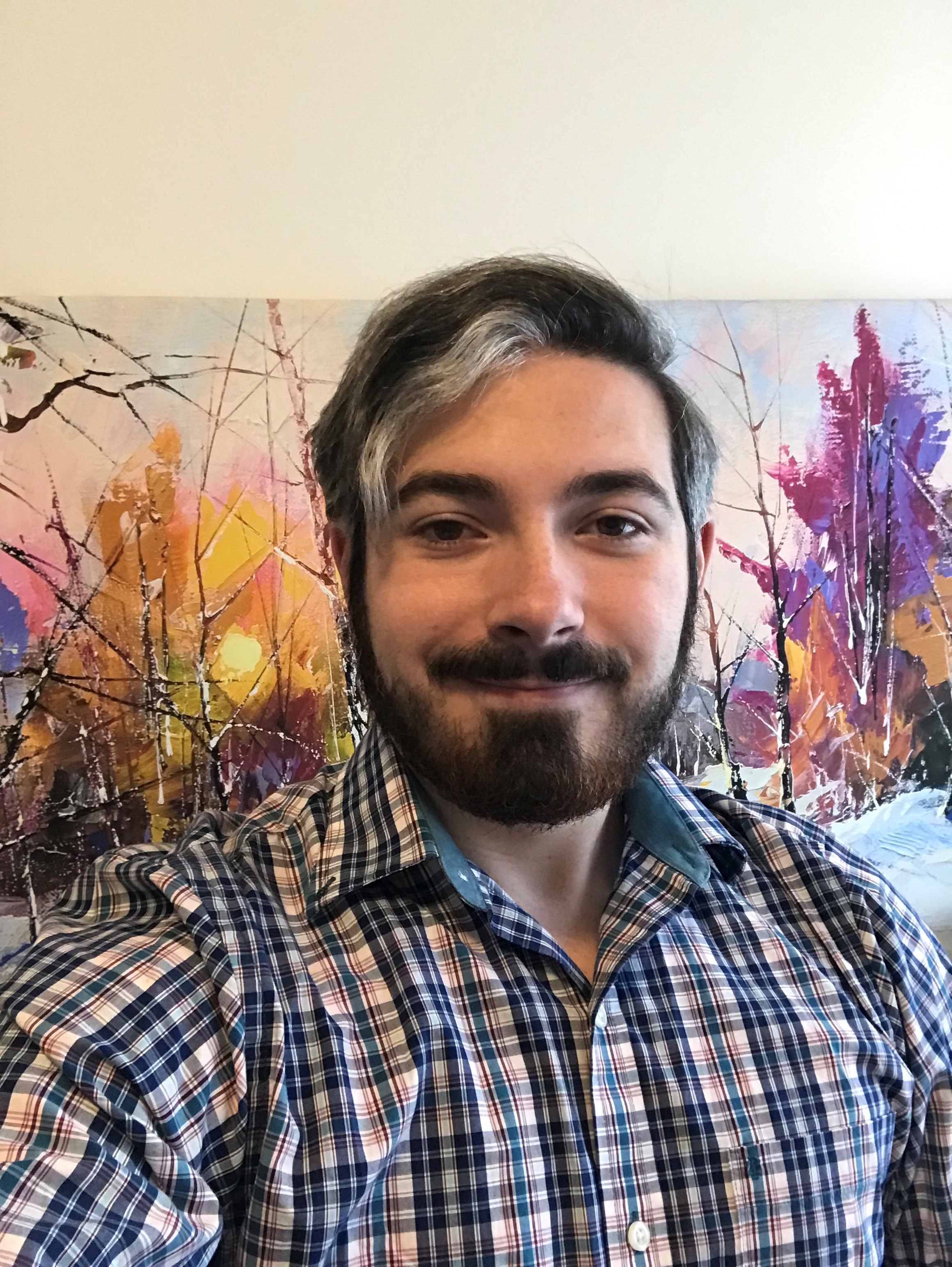 A dashing picture of AJ in front of a color splashed canvas of contrasting snowy trees.